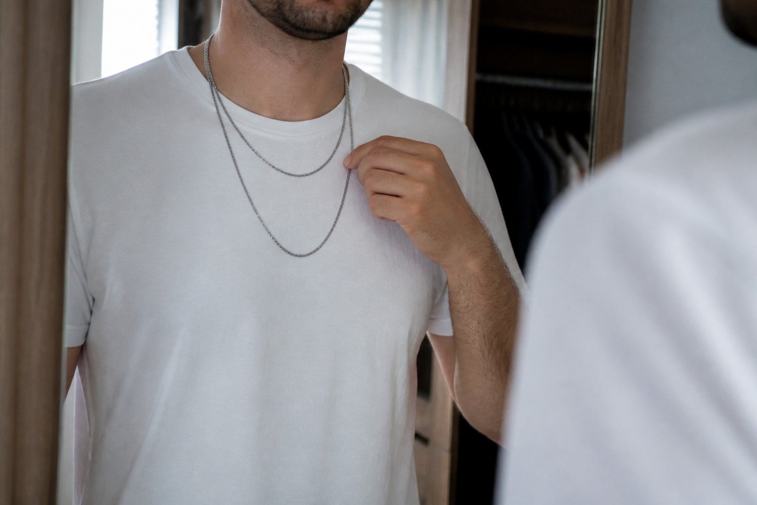 Hombre comparando dos longitudes de collar sobre una camiseta lisa
